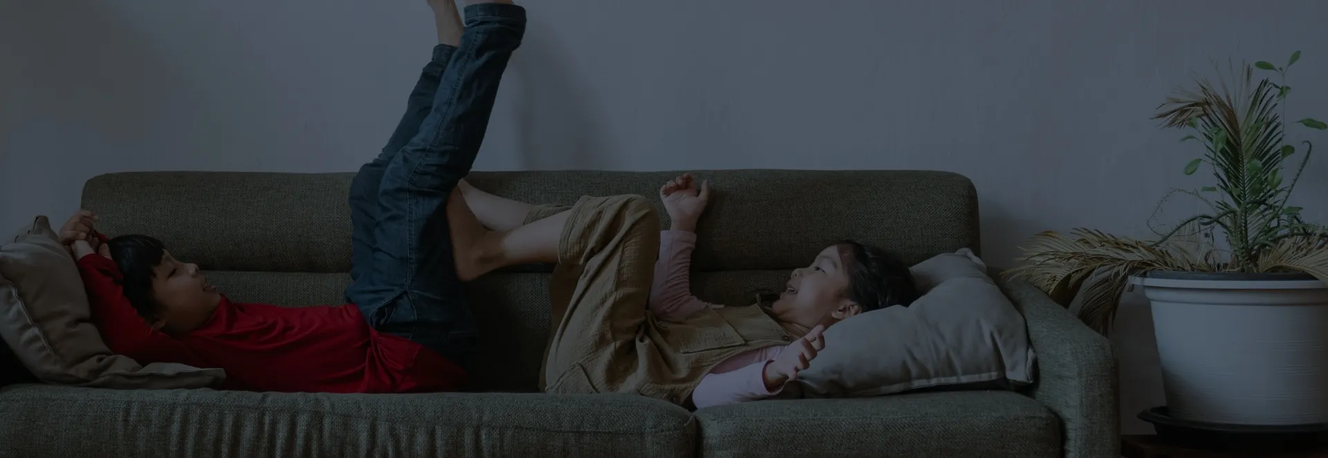 A background image showing two children playing happily on a sofa together.