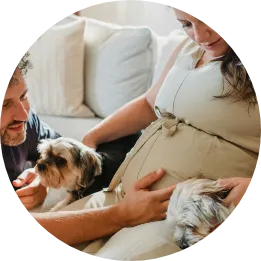 A round image showing a pregnant lady with her partner and dogs sitting on a sofa.