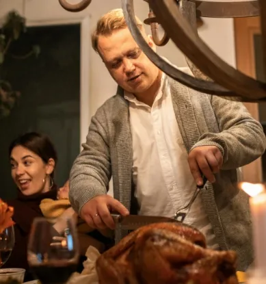 A man carving a turkey surronded by happy friends and relatives.