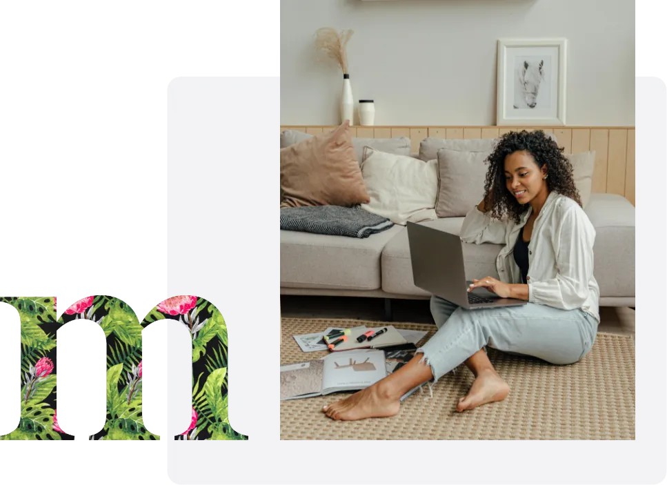 A lady sitting on the floor leaning against a sofa working on a laptop.